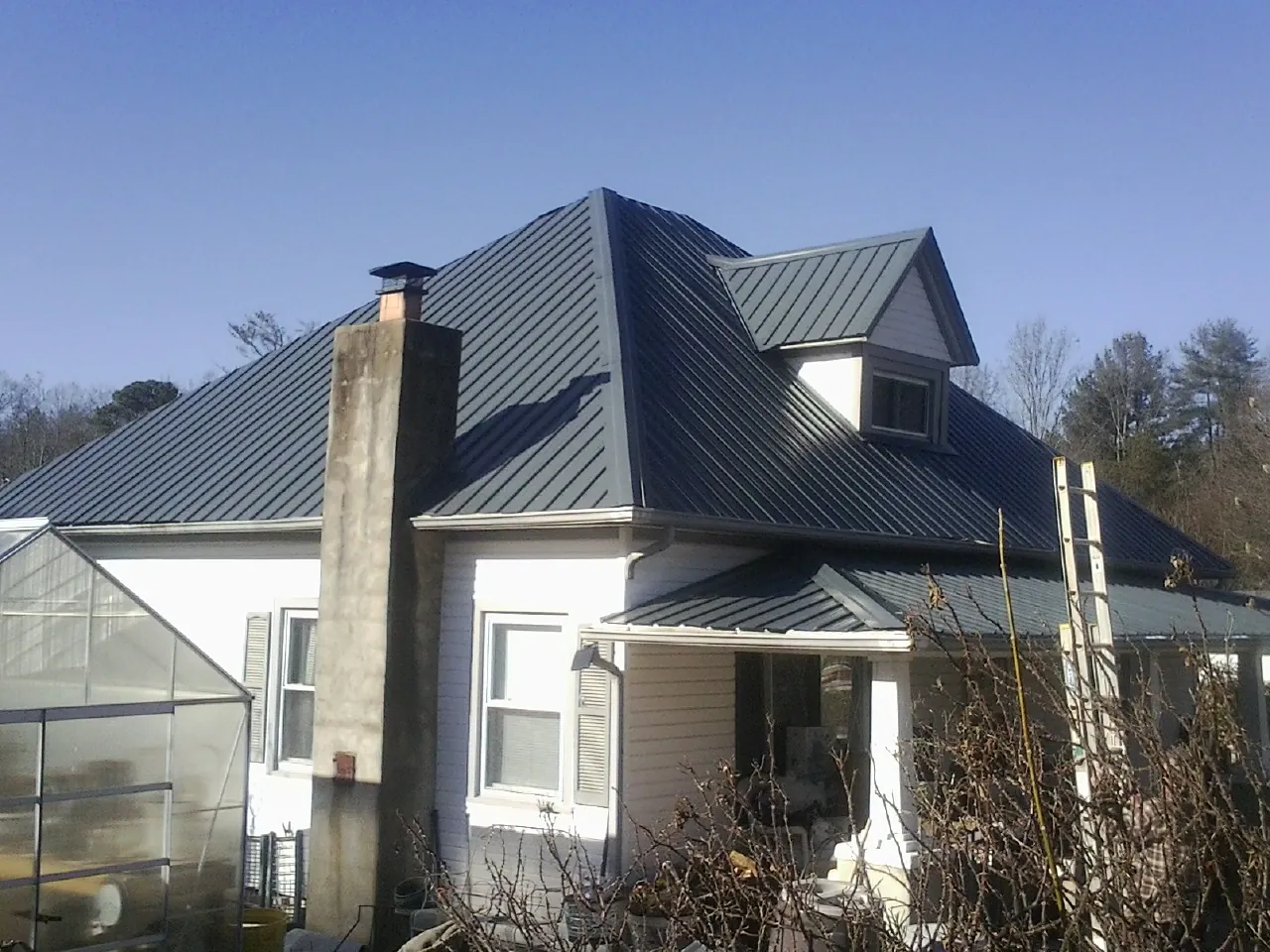 Dark blue standing seam metal roof on a white farmhouse with dormer — Slate & Tile Roof Repair by Roofing Brothers in Lumberton