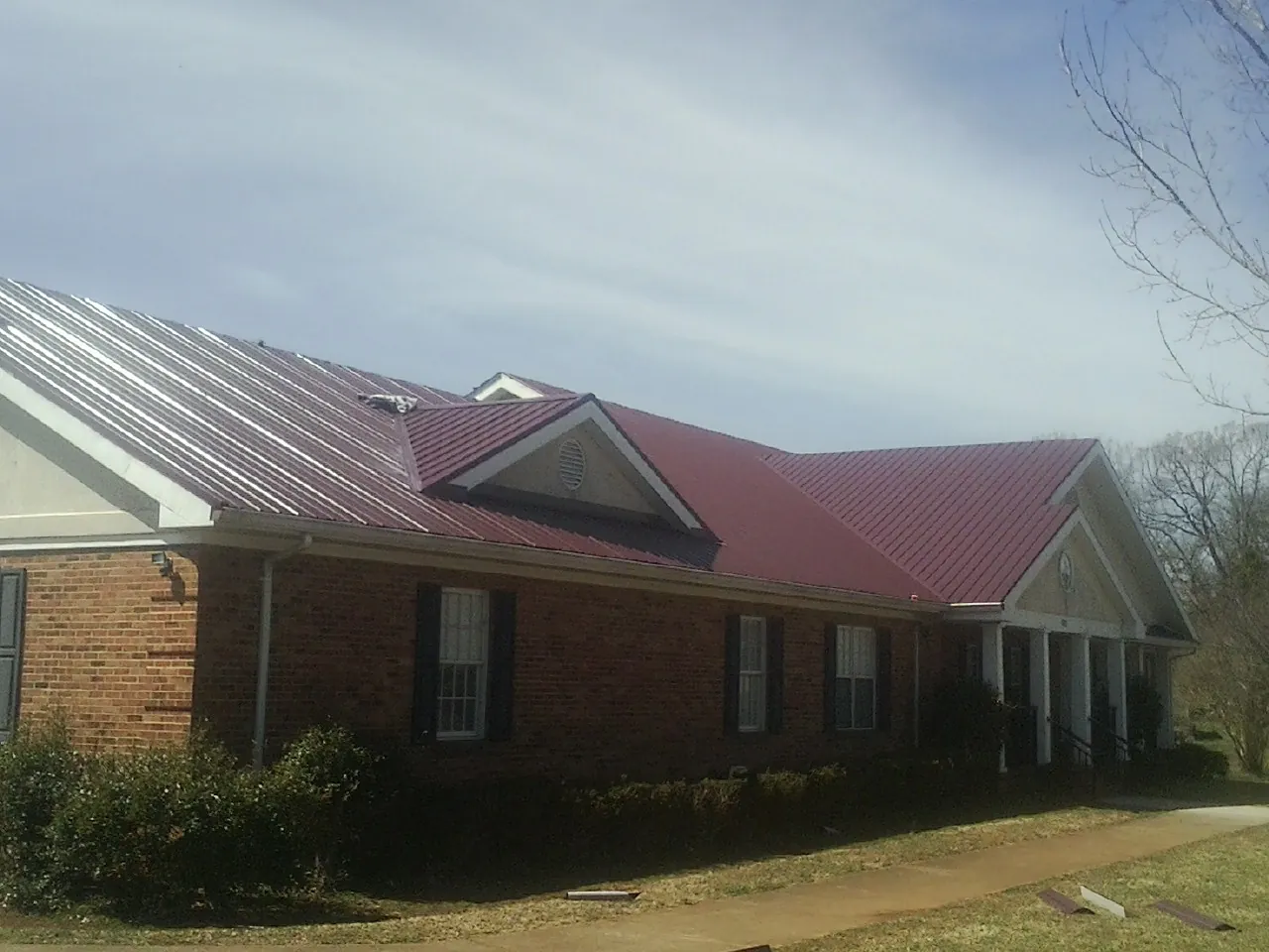 Red metal roof with gabled entries on a long brick building, from a Hail Damage Roof Repair job in Lumberton
