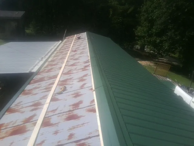 Old rusted panels beside newly installed green metal roofing — Wind Damage Roof Repair by Roofing Brothers in Lumberton